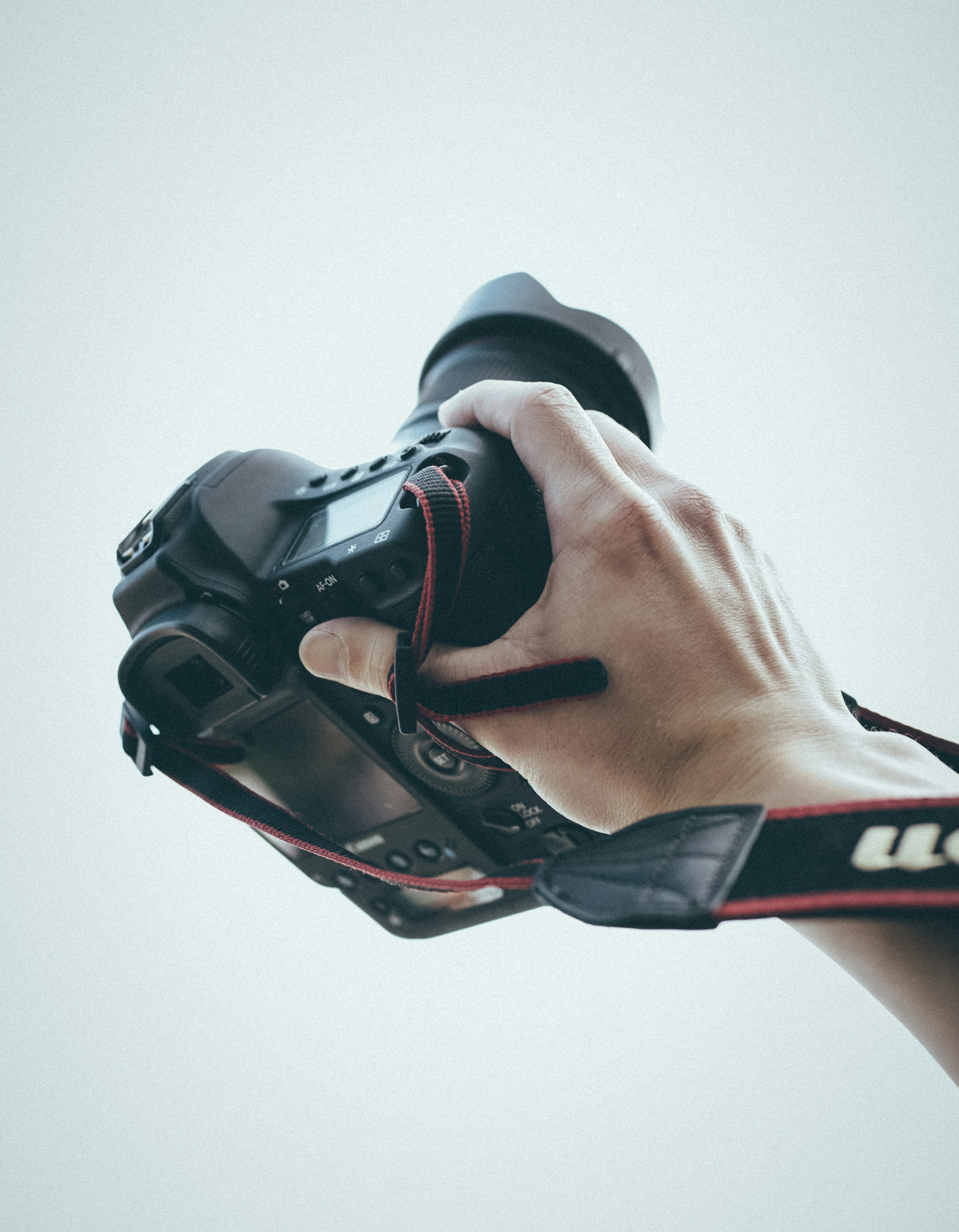 Camera body and lens held in hand against open sky